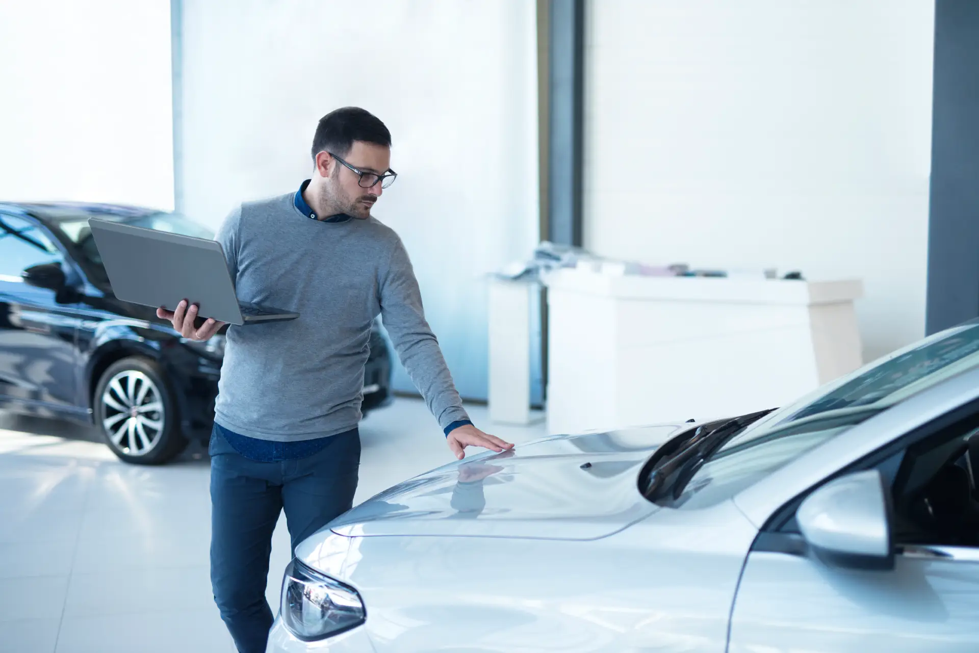 car-salesperson-with-laptop-checking-vehicle-specifications-local-dealership-showroom